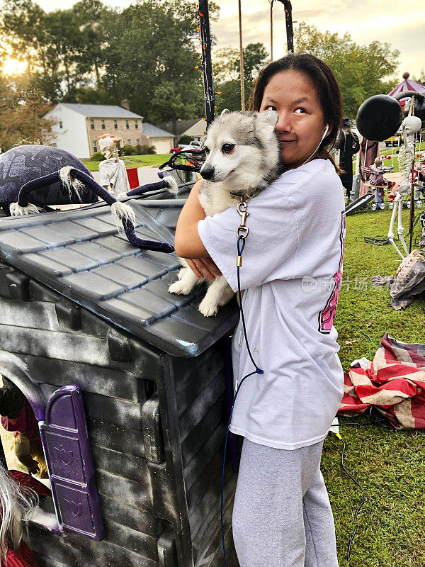 Asian teen snuggles with her dog after helping her family decorate their front yard for Halloween